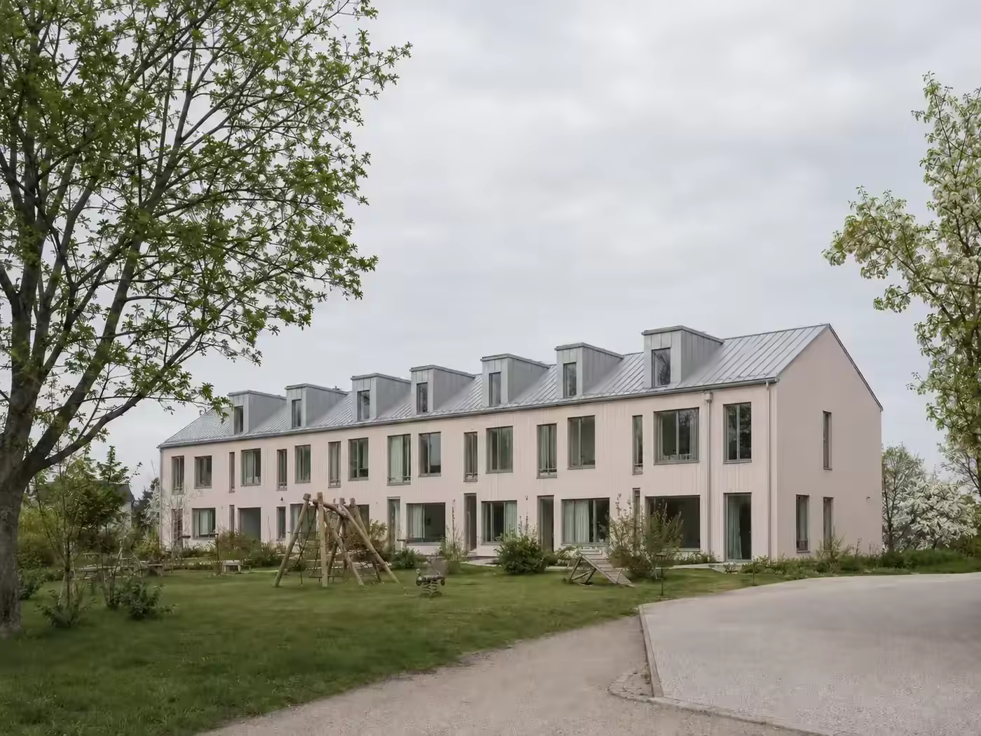 Wohnbebauung an der Bayernwerkstraße mit heller Holzfassade und gemeinschaftlichem Garten